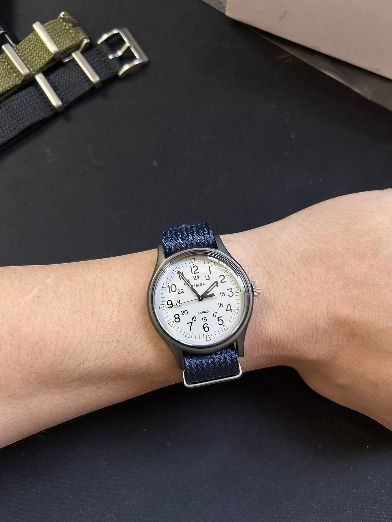 Reloj Timex MK1 de DEL MORAL | RELOJES con esfera blanca, caja de aluminio y correa de nylon azul en la muñeca.